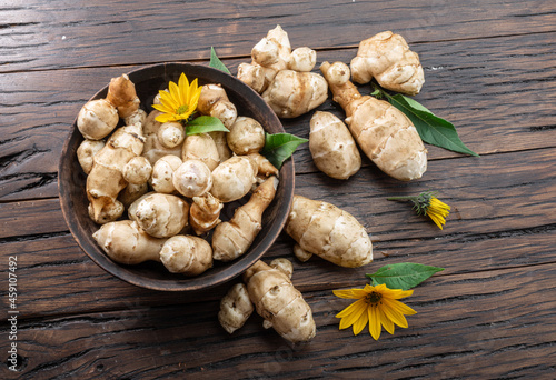 Jerusalem artichoke roots with leaves and flower of Jerusalem artichoke on a old wooden table.