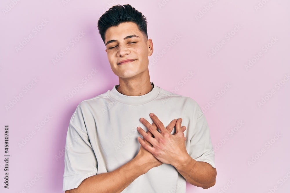 Young hispanic man wearing casual white t shirt smiling with hands on chest, eyes closed with grateful gesture on face. health concept. Young hispanic man wearing casual white t shirt smiling with hands on chest, eyes closed with grateful gesture on face. health concept.