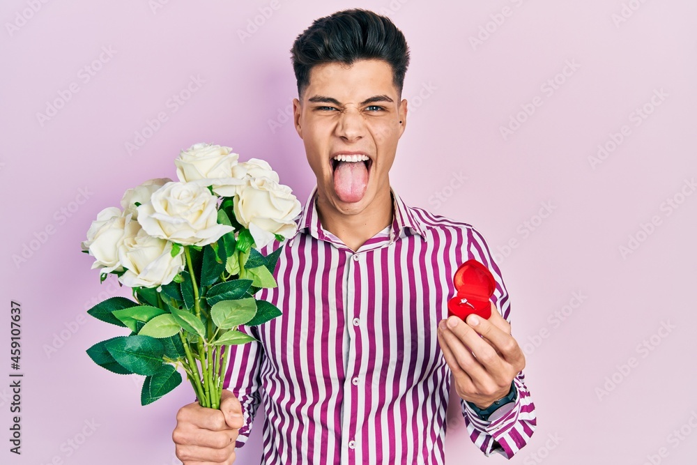 Young hispanic man holding bouquet of flowers and wedding ring sticking tongue out happy with funny expression. Young hispanic man holding bouquet of flowers and wedding ring sticking tongue out happy with funny expression.