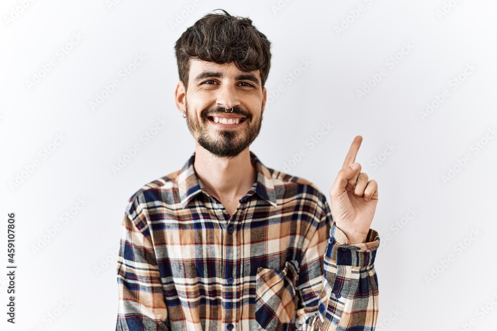 Hispanic man with beard standing over isolated background with a big smile on face, pointing with hand and finger to the side looking at the camera. Hispanic man with beard standing over isolated background with a big smile on face, pointing with hand and finger to the side looking at the camera.