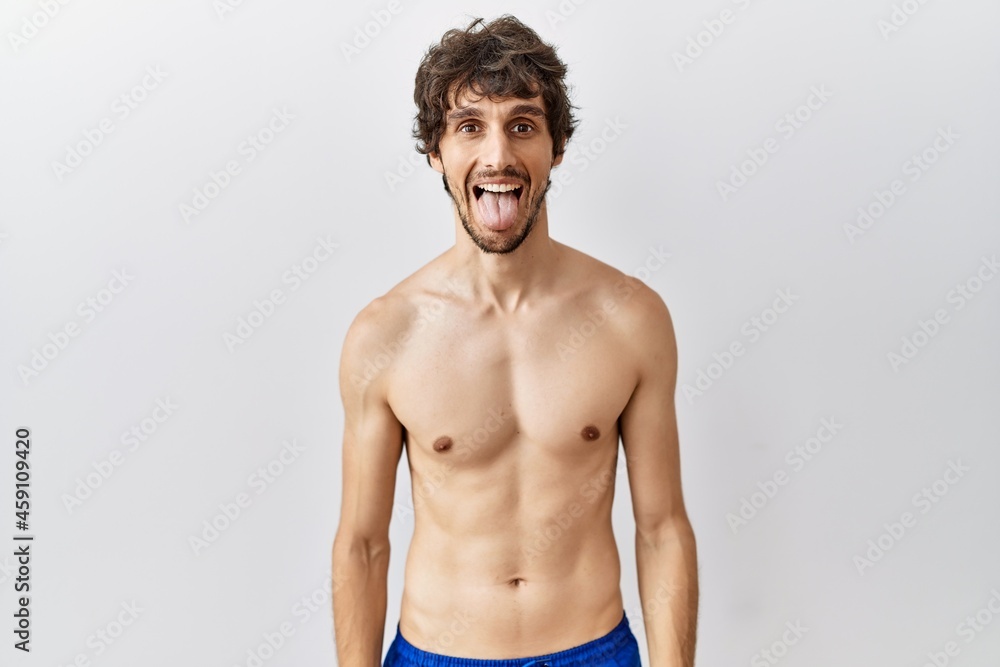 Young hispanic man standing shirtless over isolated, background sticking tongue out happy with funny expression. emotion concept.