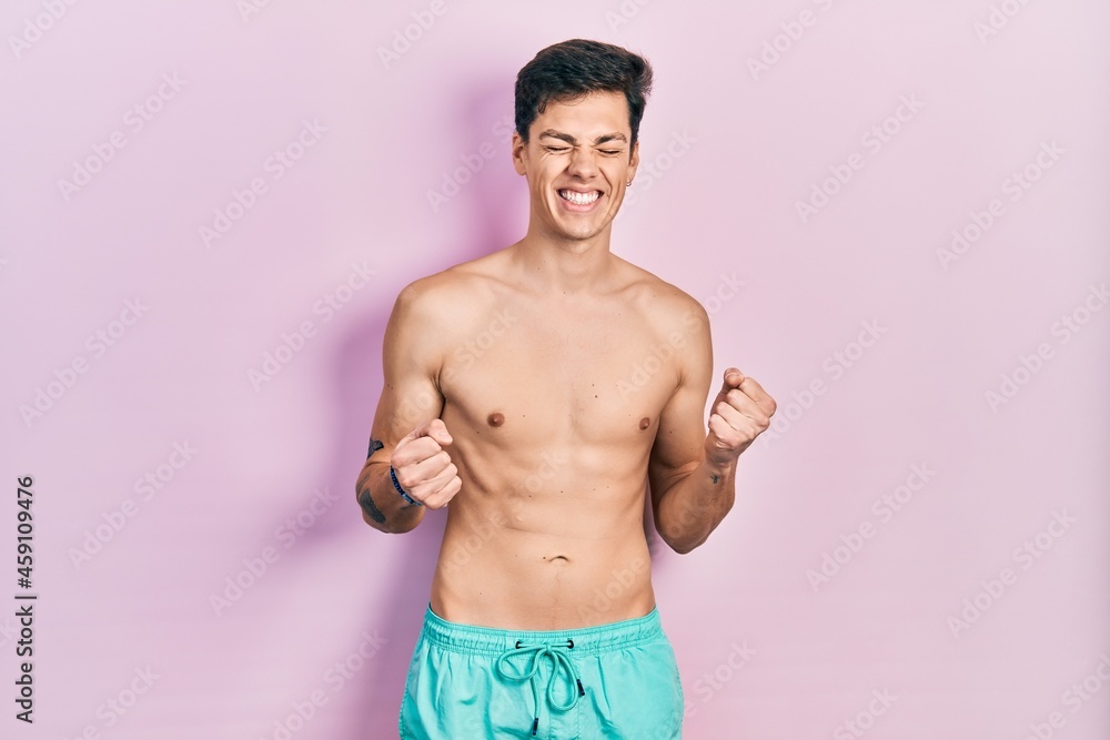 Fototapeta premium Young hispanic man wearing swimwear shirtless excited for success with arms raised and eyes closed celebrating victory smiling. winner concept.