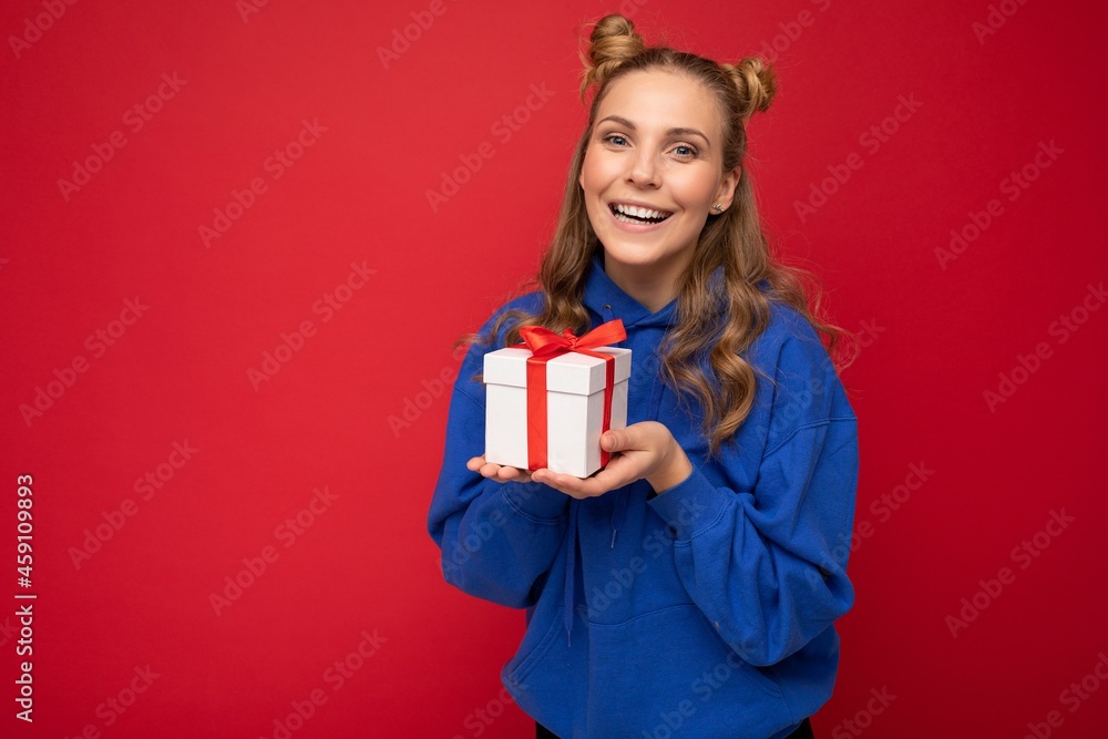Beautiful happy young blonde woman isolated over colourful background wall wearing stylish casual clothes holding gift box and looking at camera Beautiful happy young blonde woman isolated over colourful background wall wearing stylish casual clothes holding gift box and looking at camera