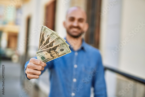 Young hispanic man smiling happy holding dollars at the city.
