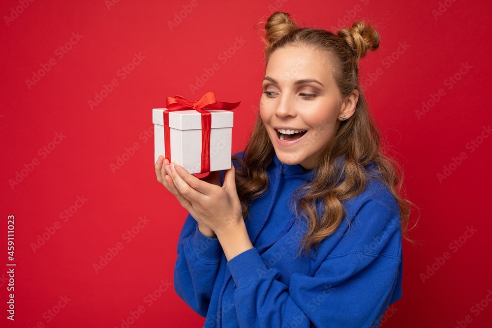 Beautiful happy young blonde woman isolated over colourful background wall wearing stylish casual clothes holding gift box and looking to the side Beautiful happy young blonde woman isolated over colourful background wall wearing stylish casual clothes holding gift box and looking to the side