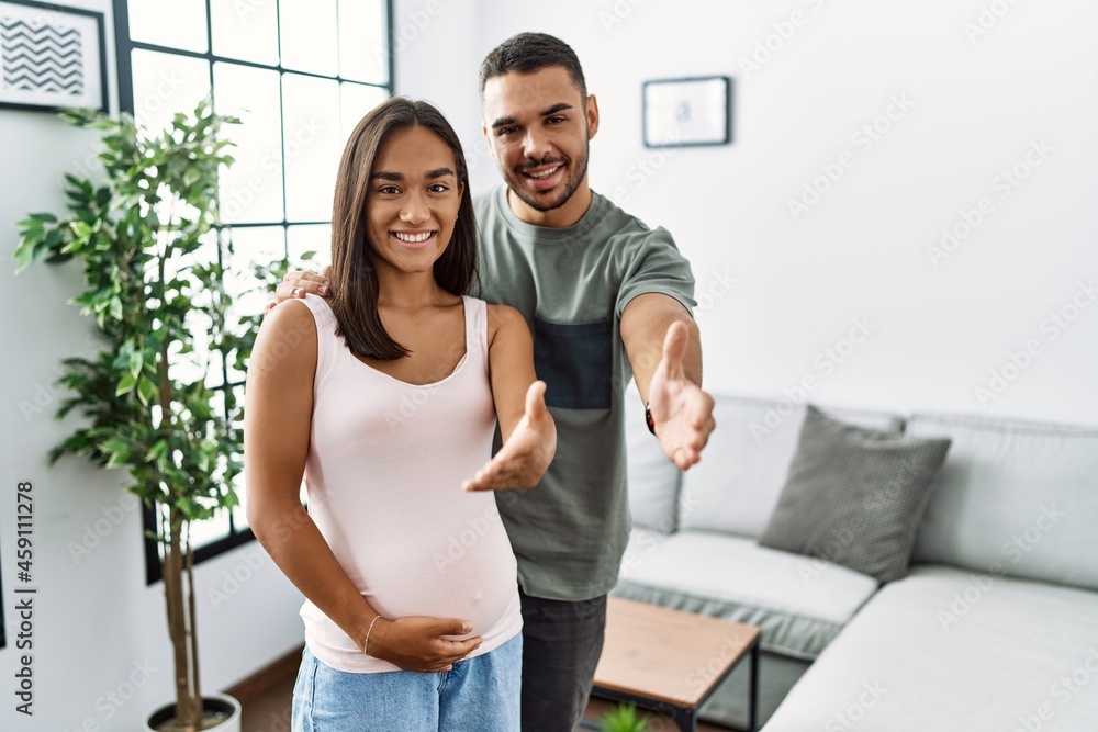 Young interracial couple expecting a baby, touching pregnant belly smiling friendly offering handshake as greeting and welcoming. successful business. Young interracial couple expecting a baby, touching pregnant belly smiling friendly offering handshake as greeting and welcoming. successful business.