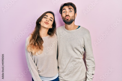 Young hispanic couple wearing casual clothes looking at the camera blowing a kiss on air being lovely and sexy. love expression.