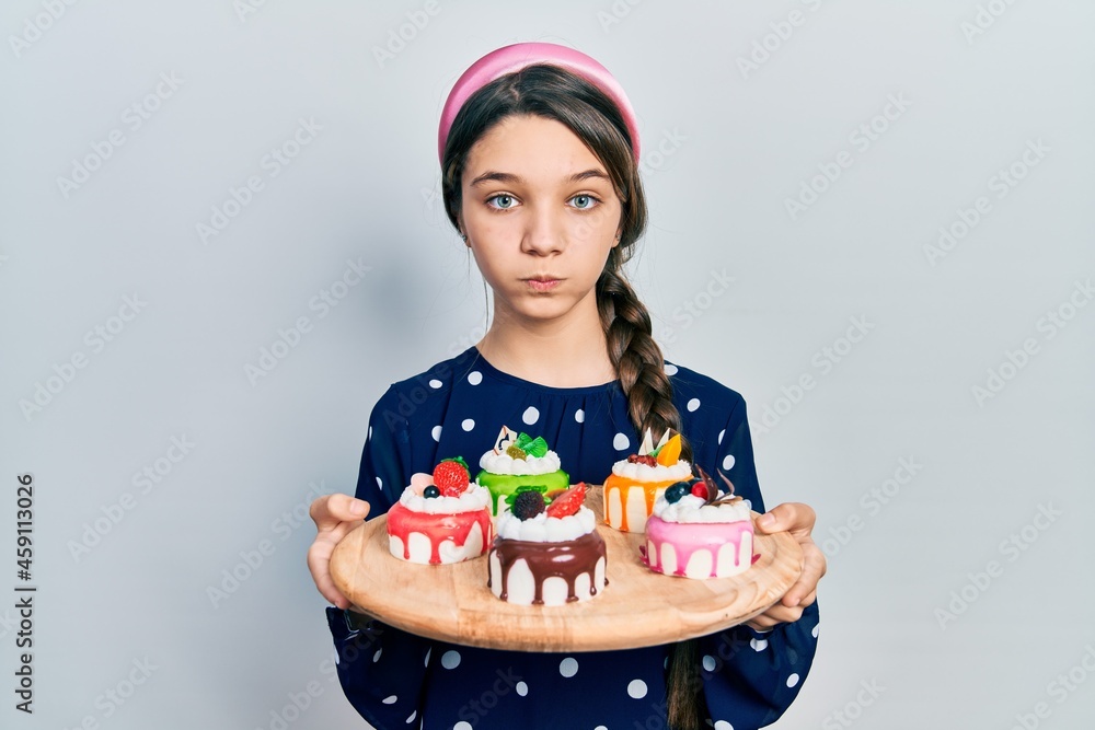 Young brunette girl holding sweet pastries puffing cheeks with funny face. mouth inflated with air, catching air. Young brunette girl holding sweet pastries puffing cheeks with funny face. mouth inflated with air, catching air.