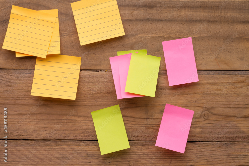 Yellow, green, pink reminder notes on a wooden board, empty space for text. Yellow, green, pink reminder notes on a wooden board, empty space for text.