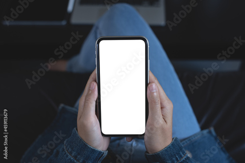 Cell phone mockup image blank white screen. Woman hand holding, using mobile phone during working on laptop computer at home.