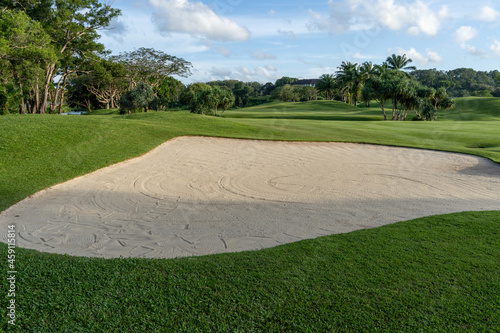The golf course sand obstacles have clear skies and beautiful natural trees
