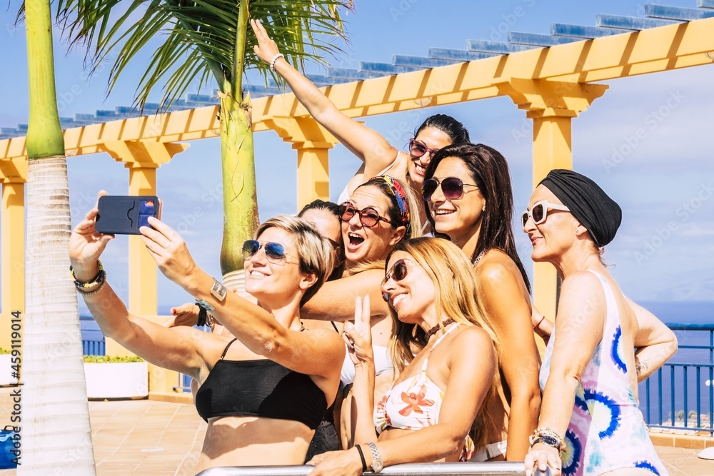 Group of female friends enjoying summer holidays in resort and taking selfie using smartphone. Women in swimsuit enjoying pool party. Attractive female friends taking photos using mobile phone camera