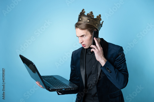 Obraz na plátně businessman with a crown on his head uses a laptop and a phone.