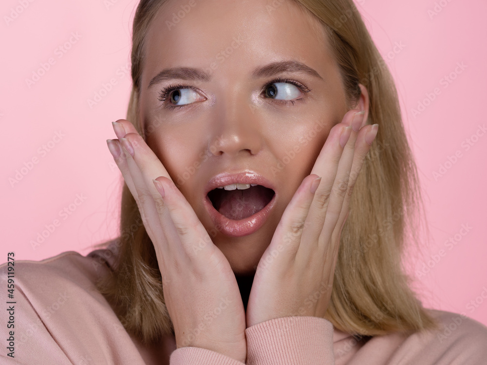 cute young blonde in a pink hoodie is shocked and surprised, says wow. cute young blonde in a pink hoodie is shocked and surprised, says wow.
