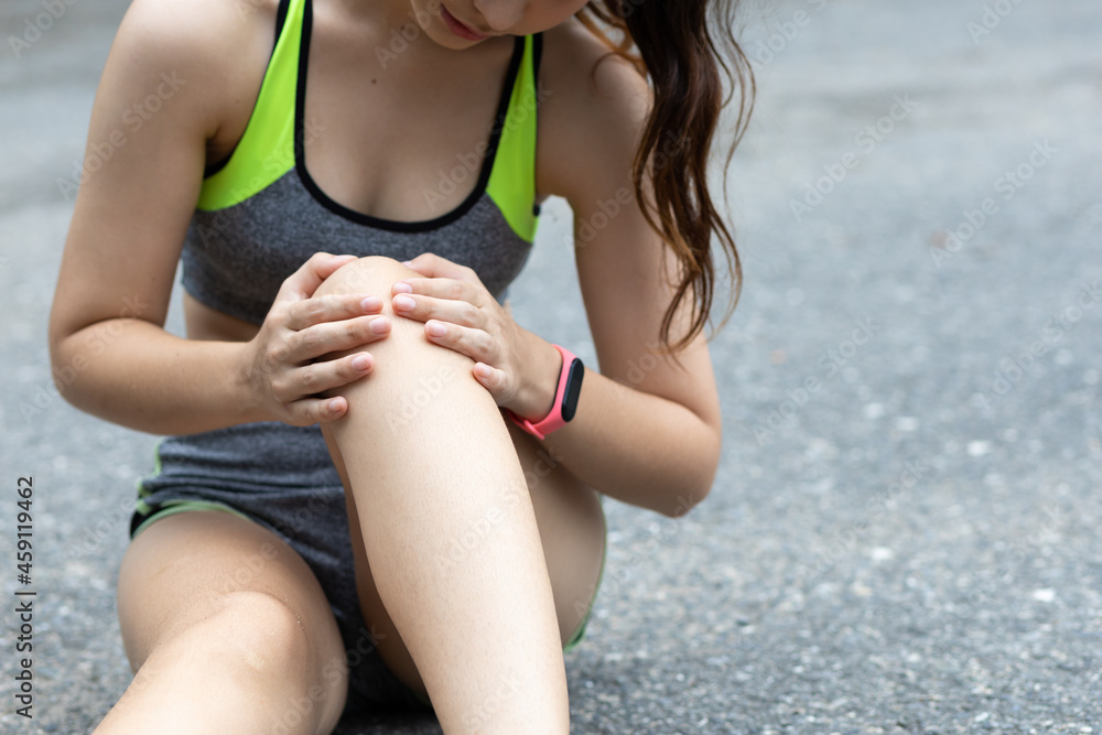 A runner sits down with a knee injury. The female athlete fell and had a bruise on her knee.
