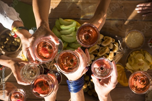 Top view of group of women hands toasting together with glasses of wine. Friends celebrating at restaurant. Top view of friends raising hands and toasting drinks glasses for celebration at hotel