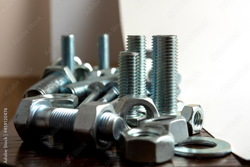 Several metal bolts and nuts on a wooden table next to a white background Several metal bolts and nuts on a wooden table next to a white background
