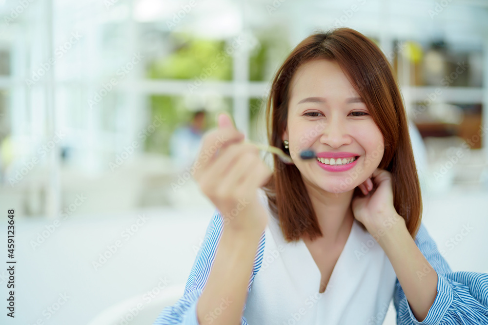A beautiful Asian portrait is taking a spoonful of cakes on the table and eating them with happy eyes and expressions in the bakery. A beautiful Asian portrait is taking a spoonful of cakes on the table and eating them with happy eyes and expressions in the bakery.