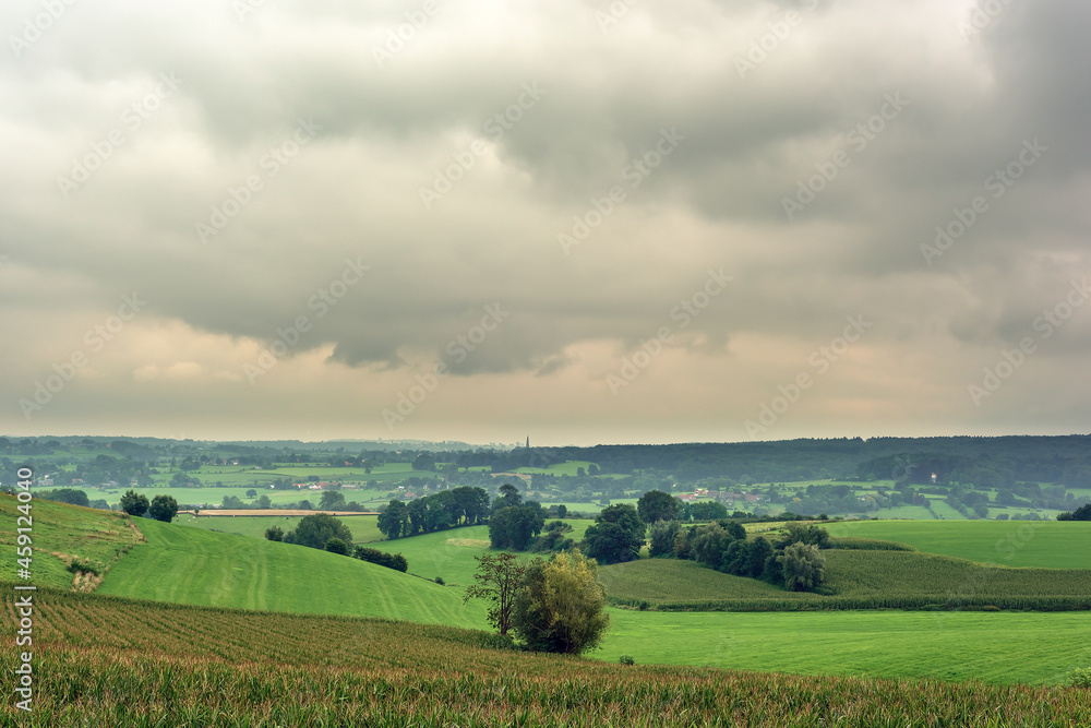 Lush hilly landscape with meadows, trees and small villages under a cloudy sky.
