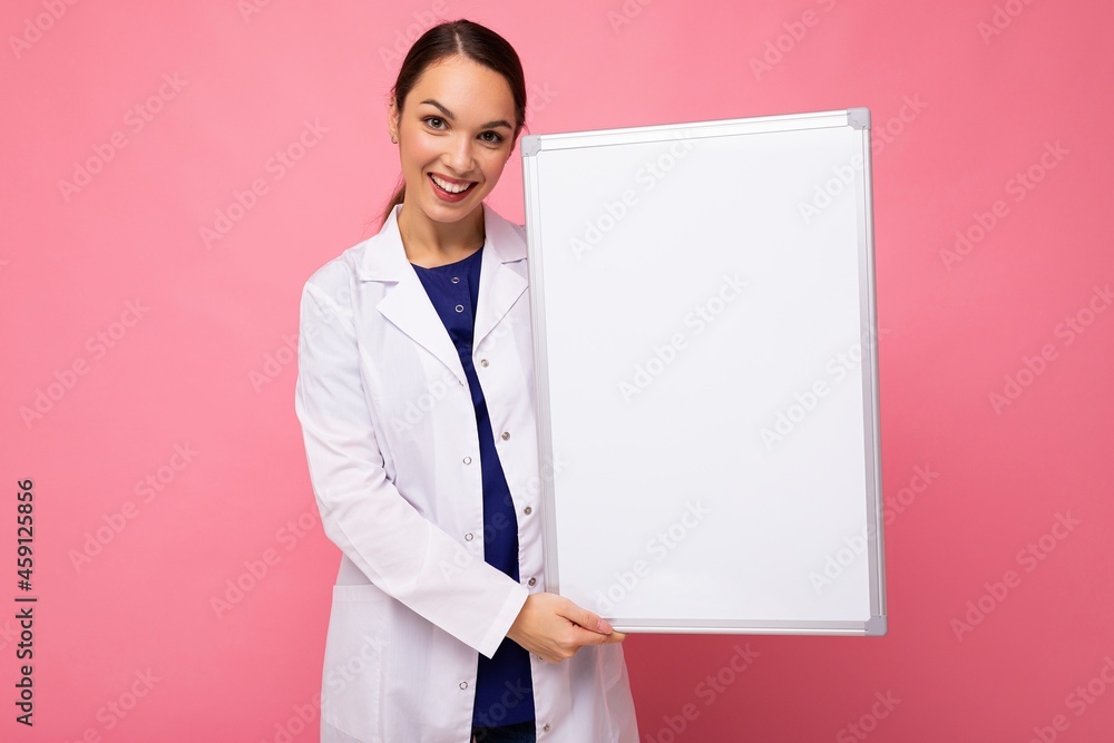 Young of beautiful happy smiling brunet woman wearing medical white coat holding white magnetic board for mockup isolated on pink background with empty space Young of beautiful happy smiling brunet woman wearing medical white coat holding white magnetic board for mockup isolated on pink background with empty space