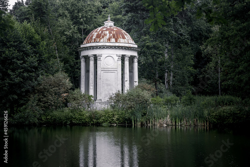 A beautiful abandoned old rotunda in the forest. Beautiful summer nature. Reflection in water. Ancient architecture.