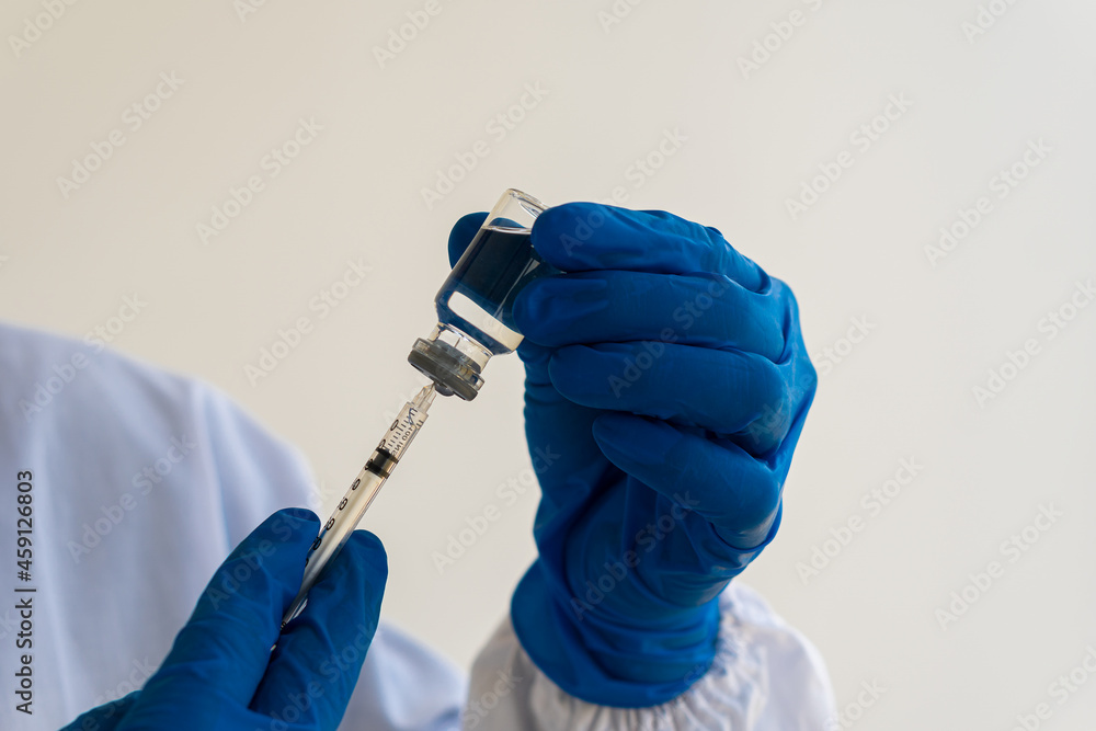 A doctor wearing blue gloves holds a bottle with vaccines and a syringe to protect against the virus. concept of medicine and health A doctor wearing blue gloves holds a bottle with vaccines and a syringe to protect against the virus. concept of medicine and health