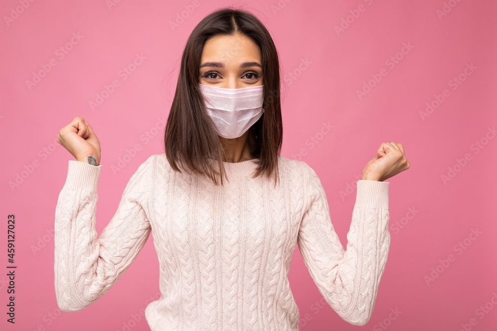 Young happy brunette woman wearing an anti virus protection mask to prevent others from corona COVID-19 and SARS cov 2 infection isolated over pink background Young happy brunette woman wearing an anti virus protection mask to prevent others from corona COVID-19 and SARS cov 2 infection isolated over pink background