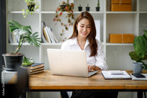 Portrait of beautiful asian young Business woman working audit and calculating expense annual financial report balance sheet statement,doing finance making notes on paper graph data checking document. © David