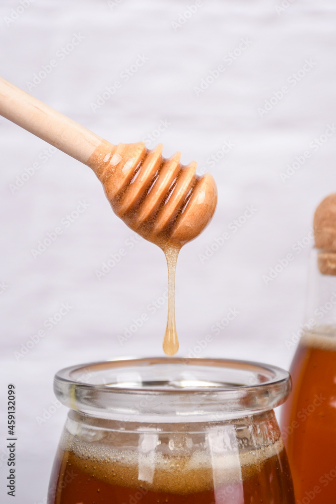 Drops of honey from a wooden spoon of honey into a glass jar of honey on a wooden placemat Drops of honey from a wooden spoon of honey into a glass jar of honey on a wooden placemat