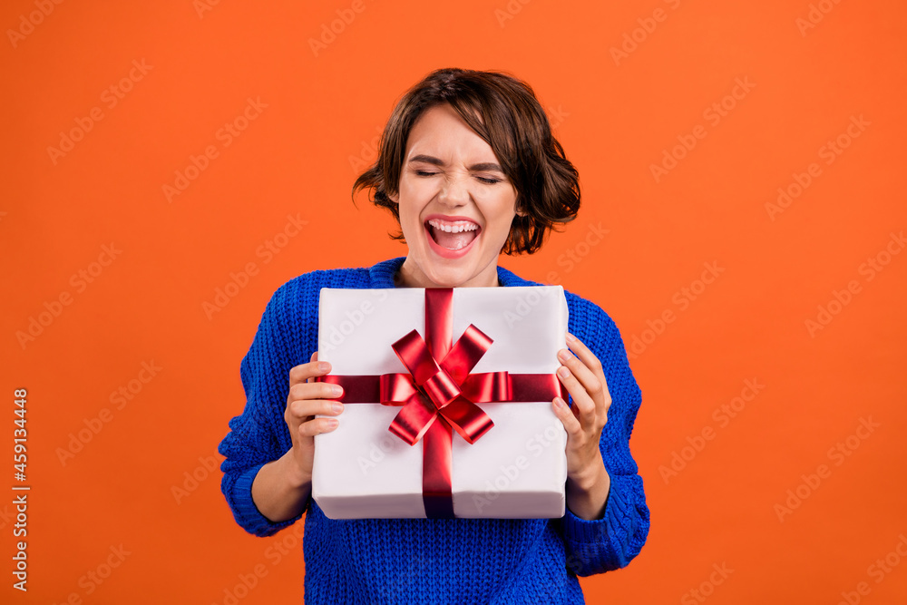 Portrait of attractive dreamy ecstatic cheerful girl holding in hands gift celebrating isolated over bright orange color background Portrait of attractive dreamy ecstatic cheerful girl holding in hands gift celebrating isolated over bright orange color background