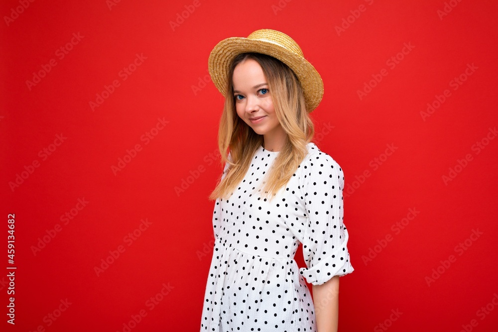 Photo shot of young beautiful cute happy blonde woman wearing casual dress and straw hat isolated over red background with copy space Photo shot of young beautiful cute happy blonde woman wearing casual dress and straw hat isolated over red background with copy space