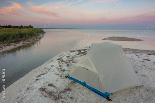 Tourist tent by the sea in the early morning. Beautiful sky with curved lines of clouds. Peace of mind, relaxation.