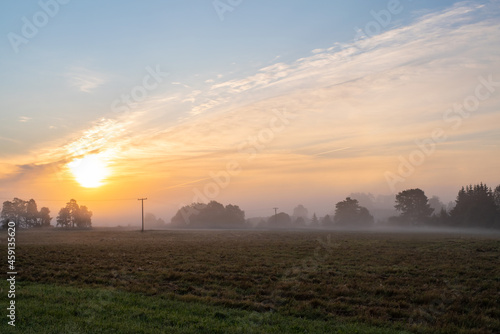 Sunrise over the meadow. Early autumn morning in the countryside. Light shining in the morning foggy field.