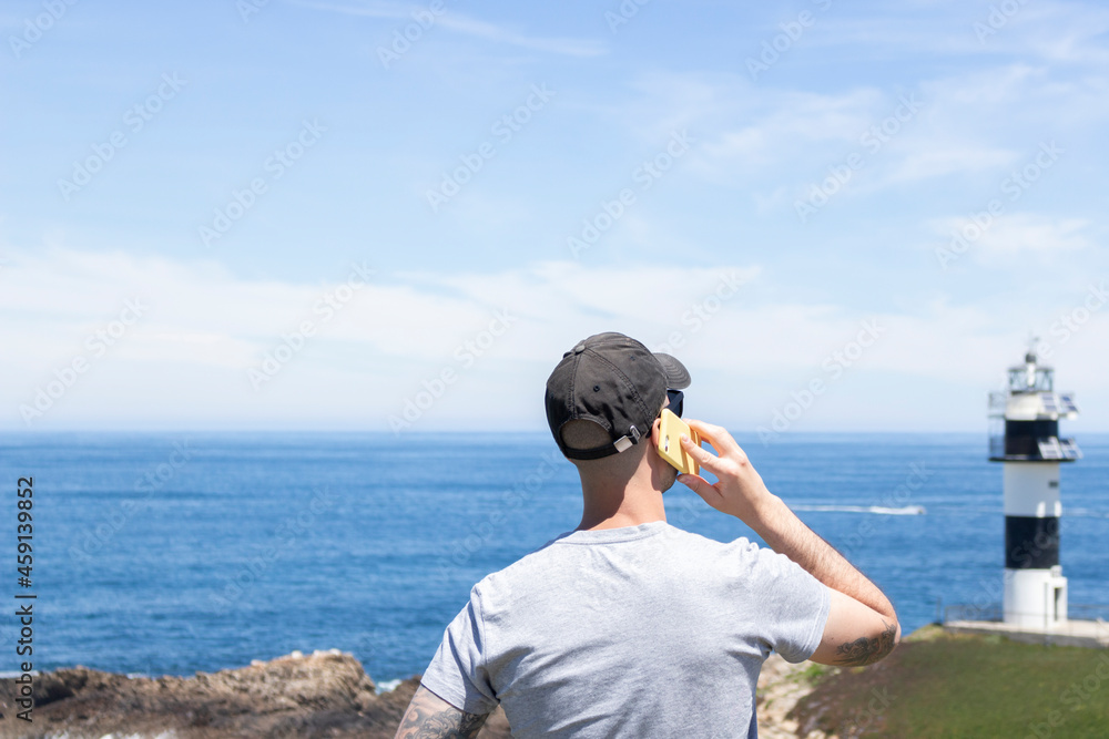 Young man talking on his cell phone from the beach, during his summer vacation