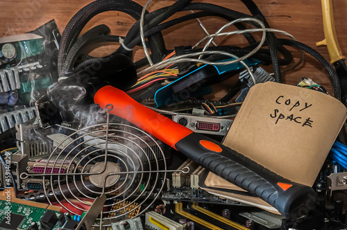 A large pile of computer components with tools. Gray smoke is streaming from the soldering iron. An open notebook with an inscription. Large hammer with an orange handle. Copy space.