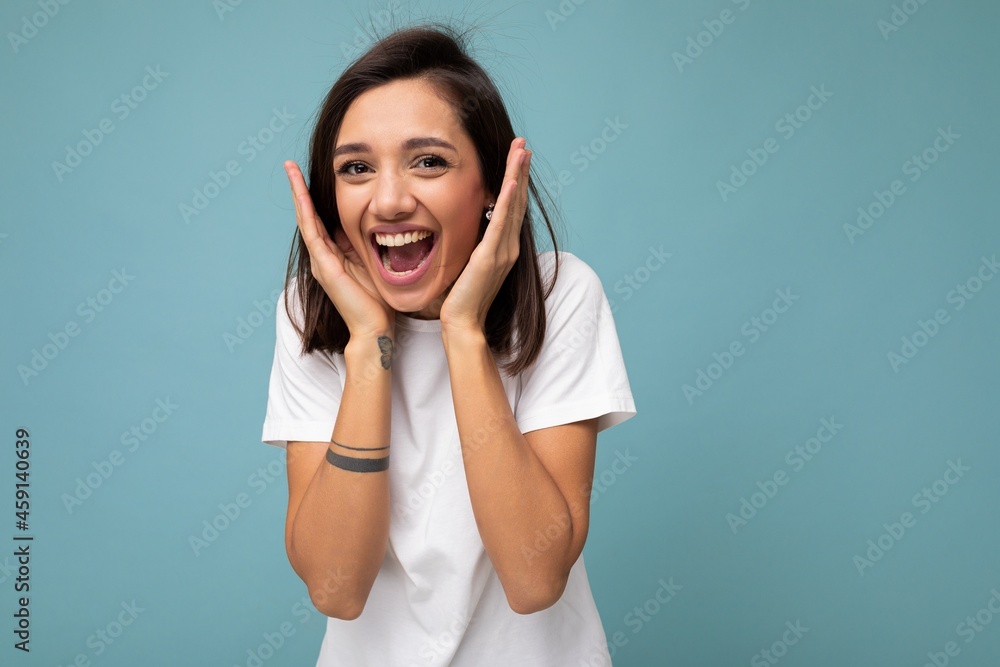 Portrait of happy positive smiling delightful young beautiful brunette woman with sincere emotions wearing casual white t-shirt for mockup isolated on blue background with copy space Portrait of happy positive smiling delightful young beautiful brunette woman with sincere emotions wearing casual white t-shirt for mockup isolated on blue background with copy space