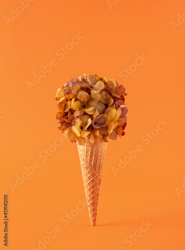Ice cream cone with fall flowers on orange background. Creatve autumn still life thanksgiving concept. photo