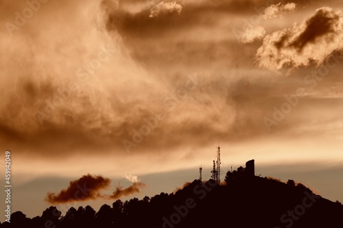 Spectacular stormy sunset over a medieval tower and a telecommunications tower on a mountain in Granada (Spain)