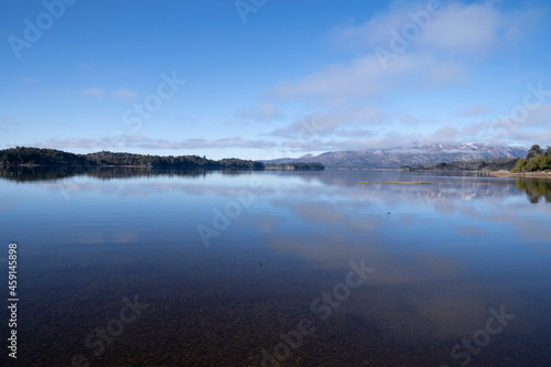 The lake in a sunny morning. Panorama view of the lake and the perfect reflection of the sky in the blue water. The Andes mountain range in the horizon.