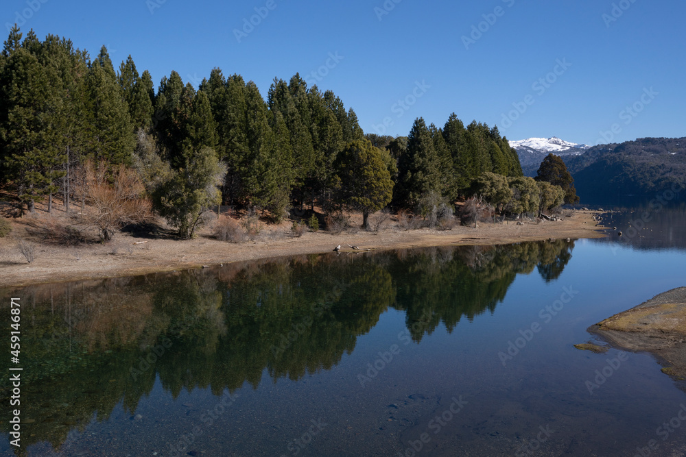 The perfect reflection of the blue sky, green forest and mountains in the lake's water surface.	