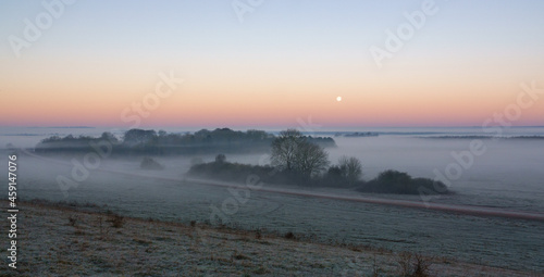 an early morning mist filled valley with the snow moon low in the sunrise sky 