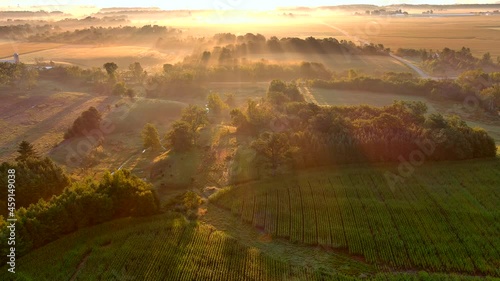 Misty rural landscape at sunrise with long shadows and beams of sunlight, aerial view.
