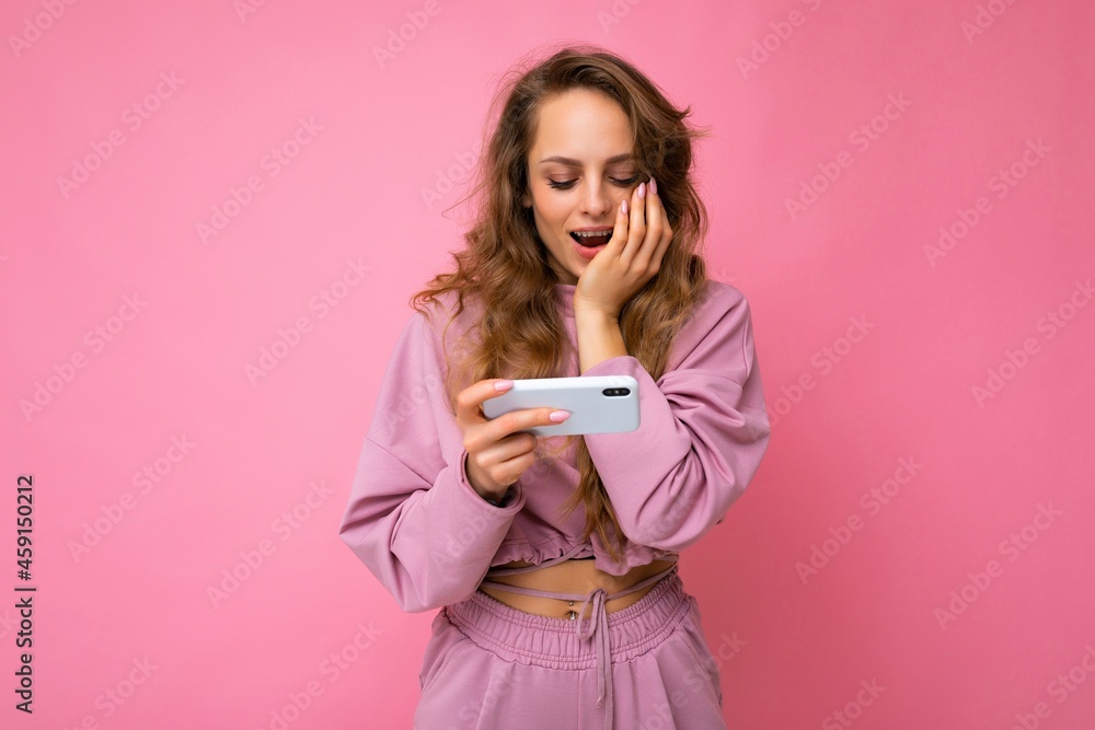 Photo shot of attractive shocked amazed positive good looking young woman wearing casual stylish outfit poising isolated on background with empty space holding in hand and using mobile phone messaging Photo shot of attractive shocked amazed positive good looking young woman wearing casual stylish outfit poising isolated on background with empty space holding in hand and using mobile phone messaging