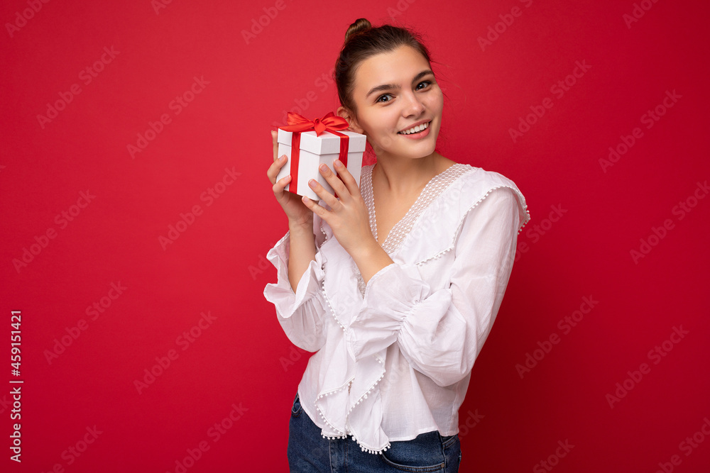 Beautiful happy young brunette woman isolated over colourful background wall wearing stylish casual clothes holding gift box and looking at camera Beautiful happy young brunette woman isolated over colourful background wall wearing stylish casual clothes holding gift box and looking at camera