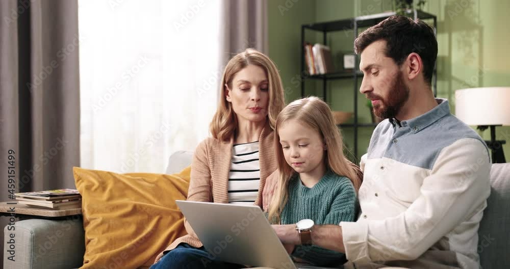 Portrait of joyful young Caucasian family with little cute girl kid sitting on sofa in room at home typing on laptop computer browsing online. Family time concept. Couple with daughter together Portrait of joyful young Caucasian family with little cute girl kid sitting on sofa in room at home typing on laptop computer browsing online. Family time concept. Couple with daughter together
