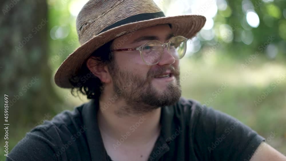 Closeup backlit portrait of man with beard, straw hat, glasses smiling and laughing in a forest. Closeup backlit portrait of man with beard, straw hat, glasses smiling and laughing in a forest.