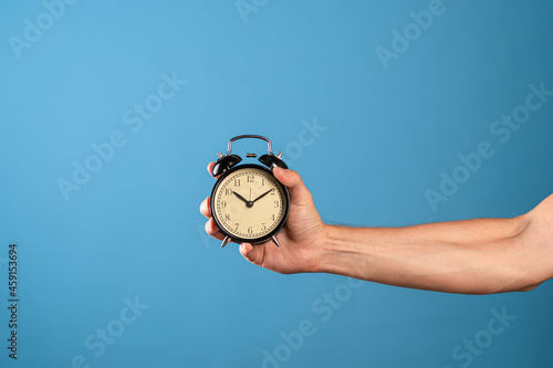 Hurry up, it's time to act, concept. A man's hand holds a vintage alarm clock, a photo on a blue background