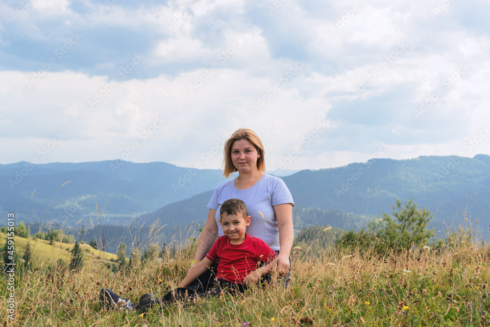 Family hiking in nature. Mother and son sit high among the hills and forest.