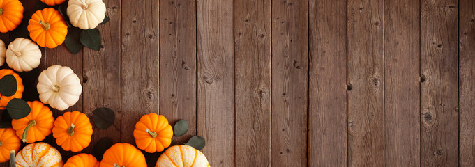 Fall corner border of pumpkins and eucalyptus leaves against a rustic dark wood banner background. Above view with copy space.