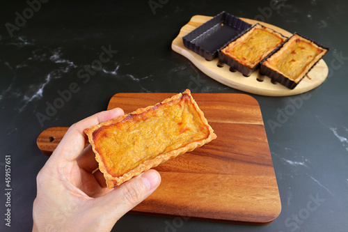 Man's Hand Holding a Fresh Baked Pumpkin Tartlet Placing on the Wooden Breadboard photo